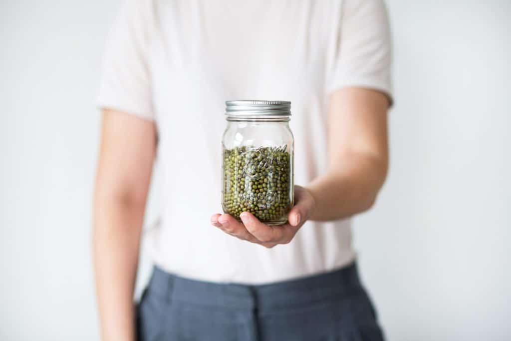 person holding clear glass jar with green peas in it