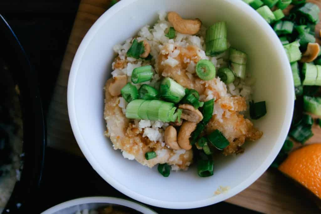 cashew orange chicken cauliflower rice green onions in a bowl