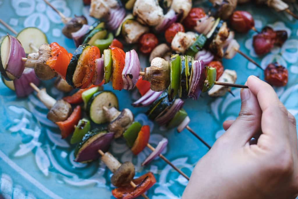 hands holding grilled veggie skewers