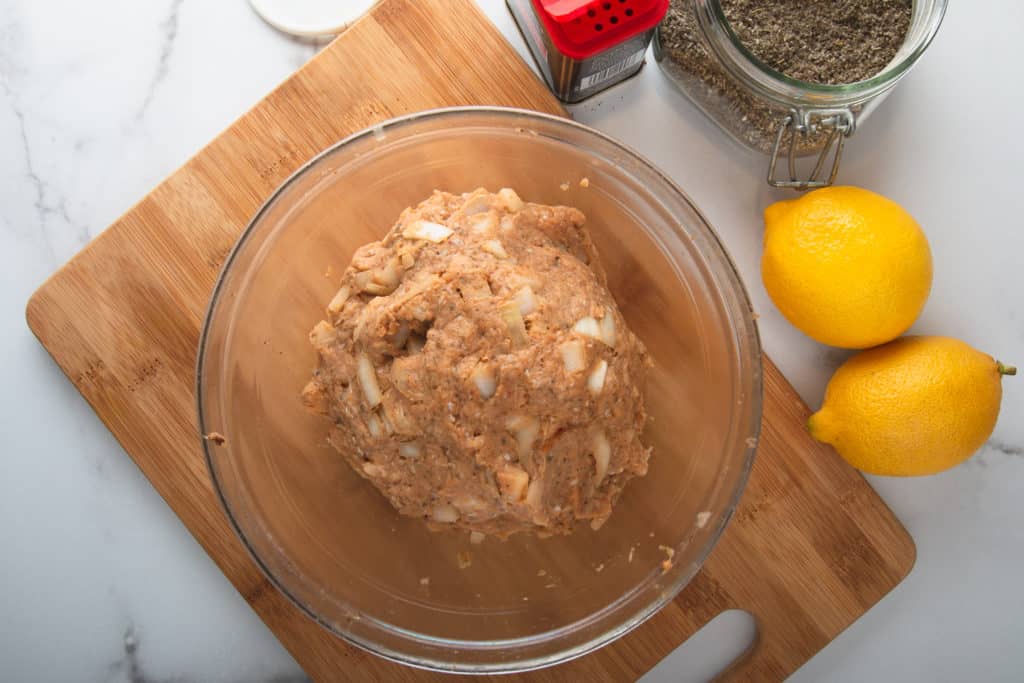 raw turkey sausage with chopped onions in a bowl with lemons and spices to the side