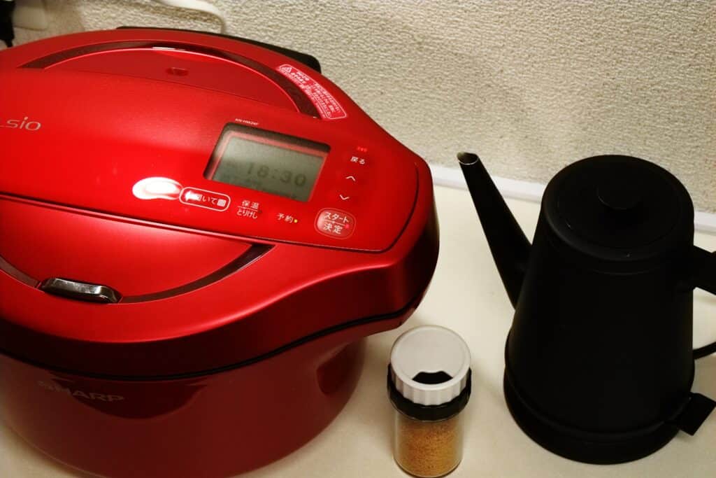 A red crock pot on a counter next to a black tea kettle